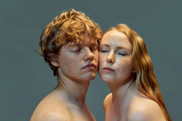 Portrait of beautiful redhead, freckled people on grey studio background. Woman and man with freckles and bare shoulders with closed eyes. Concept of natural beauty, love, relationships, fashion. Ad