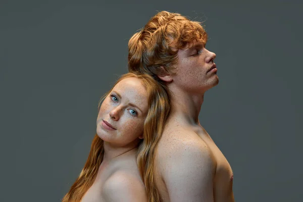 Fashionable loving redhead couple. Handsome man and beautiful woman with bare shoulders standing back to back in the studio. Concept of natural beauty, love, relationships, fashion. Ad.