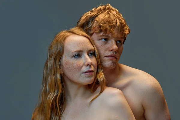 Shirtless redhead man standing closely to his redhead girlfriend who looking away against gray background. Concept of natural beauty, love, relationships, fashion. Ad. Banner