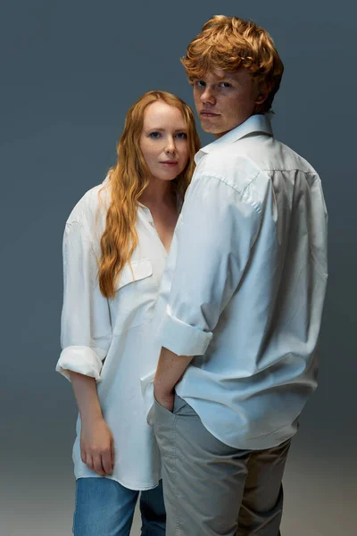 Portrait of young couple, in casual clothes, looking seriously and looking at camera on grey background. Fashion. Concept of natural beauty, love, relationships, fashion. Ad.