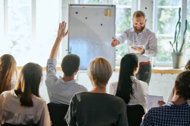 İş toplantısında erkek konuşmacı konuşma yapıyor. Konferans salonunda dinleyiciler. Hoparlörler için el kaldıran iş adamlarının arka görüşü. Eğitim, planlama, öğrenme, koçluk, iş.