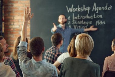 Arkadaş canlısı işletme koçu, toplantı odasında bir grup yetişkin öğrenciyle ders vererek iletişim kuruyor. Konferans, eğitim, planlama, öğrenme, koçluk, iş.