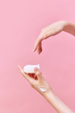 Ellerinde krema olan kadın ellerinin kavanozu. Kozmetik ürünleri kullanarak izole edilmiş pastel pembe arka plan. Vücut ve cilt bakımı, kaplıca, cilt bakımı. İlan için alanı kopyala