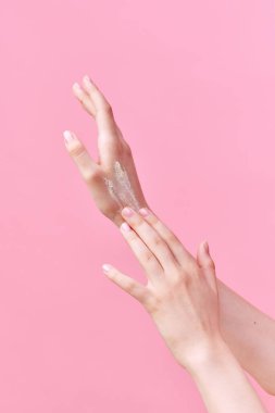 Güzel genç kadın ellerinin krem sürerken, ellerini pastel pembe arka planda ovalarken görüntüsü. Vücut ve cilt bakımı, kaplıca, cilt bakımı, tedavi. Yaşlanmaya karşı. İlan için alanı kopyala