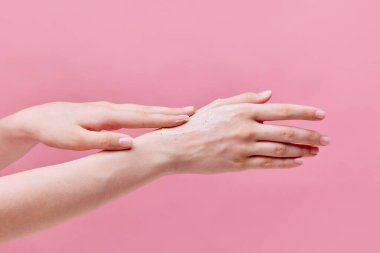 Güzel, hassas genç bir kadının yatay görüntüsü. Elleri krem sürerken, ellerini pastel pembe arka planda ovalarken. Vücut ve cilt bakımı, kaplıca, cilt bakımı, tedavi. İlan için alanı kopyala