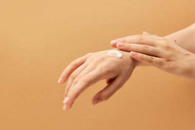 Ellerine krem sürmüş, bej arka plana krem sürmüş. Vücut ve cilt bakımı, kaplıca, cilt bakımı, tedavi. Yaşlanmaya karşı. İlan için alanı kopyala
