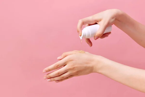 Womans hand squeezing cream, gel for hands from unmarked bottle with dispenser. Close-up, pastel pink background. Concept of body and skin care, spa, dermatology, cosmetology. Copy space for ad