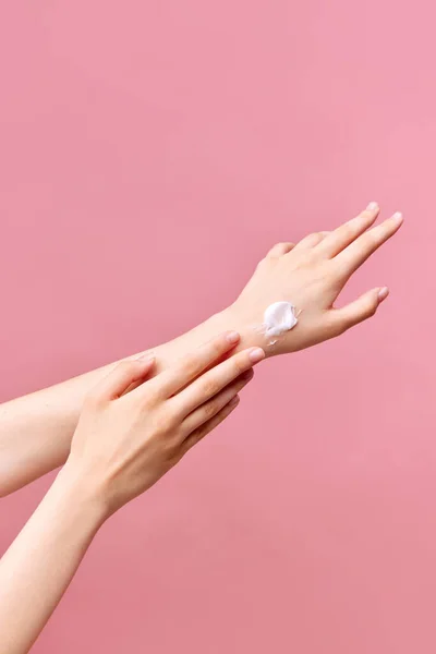 Beautiful young woman hands with cream. Woman applies cream on her hands on pastel pink background. Close-up, pastel pink background. Concept of body and skin care, spa, dermatology. Copy space for ad