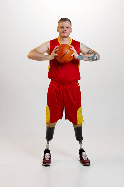 Attractive man with prosthetic leg disability standing holding orange basketball ball. Inclusive sport for people with disabilities. concept of sport, player, medical, health, body care.
