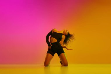 Genç esnek bir kızın ön manzara portresi. Arka planda dizlerinin üzerinde karışık ışıklarla dans ediyor. Çağdaş dans tarzı, estetik, hobi, yaratıcılık kavramı.