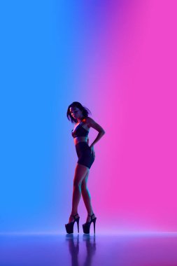 Güzel bayan dansçı siyah ve yüksek topuklu ayakkabı giyerek neon ışıkta direk dansı yapıyor. Dans yaşam tarzı kavramı, modern tarz, çağdaş, gençlik kültürü, kendini ifade etme