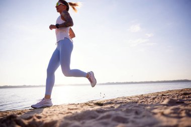 Fitness kadınının deniz kıyısında hareketli bir şekilde koştuğunu gösteren taban manzarası. Spor kadın gün batımında deniz kenarında antrenman yapıyor. spor, eğlence, sağlıklı yaşam tarzı, vücut bakımı, hobi konsepti