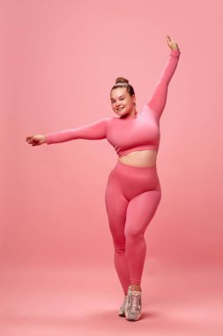 Uzun boylu, mutlu, genç, çekici ve pembe bluzlu, etkin bir kadın. Bacakları ısınıyor, antrenman yapıyor, sallanan eller, izole edilmiş stüdyo arka planı. Egzersiz, spor, motivasyon vücut pozitifliği kavramı