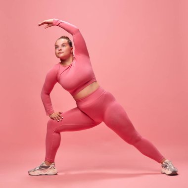 Pembe bluzlu, bacakları esnemiş, elleri ve bacakları izole stüdyo arka planında genç tombul bir kadının vücut portresi. Spor anlayışı, spor anlayışı, sağlıklı yaşam tarzı, motivasyon