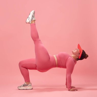 Pembe tişörtlü, bacaklı, antreman bacaklı ve izole stüdyo geçmişi olan şişman bir kadın. Tek bacak köprüsü. Spor anlayışı, spor anlayışı, sağlıklı yaşam tarzı