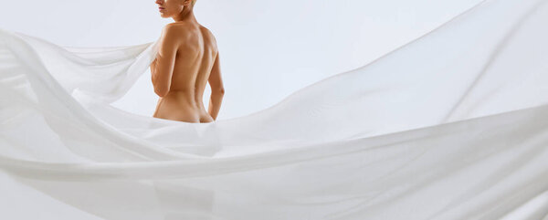Cropped portrait of young tender, fit woman covering with white transparent floating cloth on her body, hips, buttocks. Concept of natural beauty of body, health, feminine energy, cosmetology
