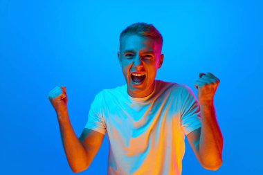 Muzaffer ve mutlu bir adamın neon ışıklı portresi el kaldırıyor, sevinç çığlıkları atıyor, zafer çığlıkları atıyor, heyecan verici duygular. Güzellik, moda, gençlik, satış, destek, hayranlar.