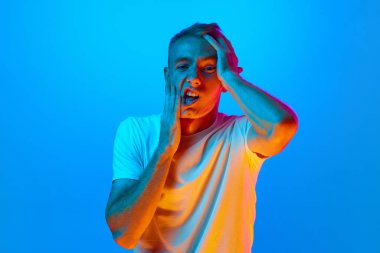 Genç bir adamın portresi, mavi stüdyonun arka planında neon ışığı altında çalışan, yüzü örten yorgun, depresyon ve üzüntü, sorun için üzgün ve tedirgin. İnsan duyguları kavramı, yüz ifadesi
