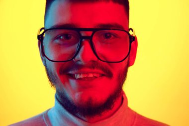 Gülümseyen yakışıklı gencin yakın portresi, sarı arka planda kırmızı ışık ve filtre ile izole edilmiş öğrenci. Mutlu, neşeli adam. Güzellik anlayışı, insani duygular, yüz ifadesi, gençlik. Ad