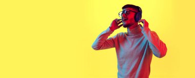 Kulaklıklı yakışıklı genç adam müzik dinliyor ve sarı arka planda kırmızı ışıkta, filtreli şarkı söylüyor. İnsani duygular kavramı, rahatlık, rahatlama. Pankart. Poster. İlan için alanı kopyala.