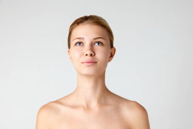 Çekici bir kızın portresi, pürüzsüz, bakımlı, güzel bir cilde sahip. Gri stüdyo arka planında izole bir şekilde yukarı bakıyor. Cilt bakımı kavramı, doğal güzellik, kozmetik ve kozmetik, spa