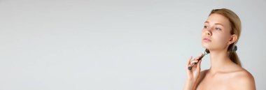 Güzel ve pürüzsüz cilt masajı yapan genç bir kız. Gri stüdyo arka planında izole edilmiş bir paten. Cilt bakımı kavramı, doğal güzellik, kozmetik ve kozmetik, spa. Pankart