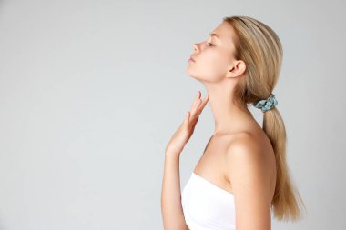 Gri stüdyo arka planında izole edilmiş pürüzsüz ciltli ve mükemmel yüz şekli olan çekici sarışın kızın yan görünümü. Cilt bakımı kavramı, doğal güzellik, kozmetik ve kozmetik, spa