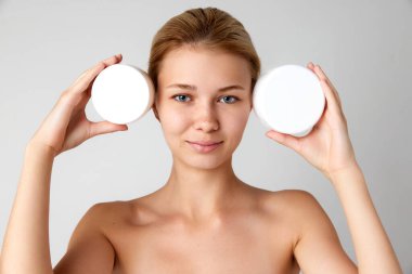 Yüzü ve vücut nemlendirici kremleri gri stüdyo arka planına izole edilmiş, iyi korunmuş, güzel bir kız. Cilt bakımı kavramı, doğal güzellik, kozmetik ve kozmetik, spa