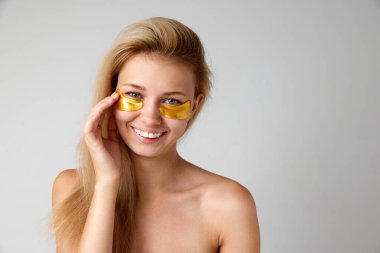 Gri stüdyo arka planında izole edilmiş göz bantları kullanarak cildini korumuş çekici bir genç kızın portresi. İçecek bir şeyler. Cilt bakımı kavramı, doğal güzellik, kozmetik ve kozmetik, spa