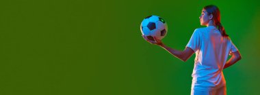 Genç bir kızın arka plan görüntüsü. Üniformalı futbolcu yeşil stüdyo arkaplanının üzerinde neon ışıkta duruyor. Profesyonel spor kavramı, rekabet, oyun, eğitim, gençlik, aksiyon, reklam