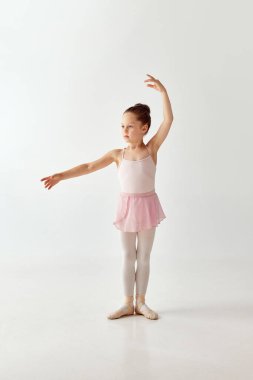 Rose Tutu bale elbisesi giymiş, beyaz bacaklı, beyaz bacaklı, beyaz arka planda el ele tutuşmuş küçük, sevimli bir anaokulu balerin kızı portresi. Güzellik kavramı, moda, hobi, kendini ifade etme