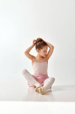 Küçük sevimli balerin kız portresi beyaz stüdyo arka planında beyaz bacaklı, tutu bale elbisesiyle saç demetini düzeltiyor. Güzellik kavramı, moda, hobi. Ad