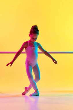 Küçük narin bir çocuk balerin kızı portresi sivri uçlu ayakkabıyla barre 'nin yanında karışık neon ışıkta poz veriyor. Kişilik gelişimi. Sanat, güzellik, moda, hobi, aksiyon kavramı. ad