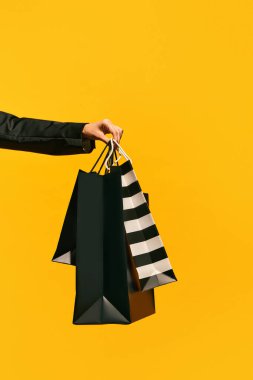 Satış teklifi. Kara Cuma. Alışveriş teslimatı. Parlak sarı arka planda izole edilmiş siyah çantalar taşıyan bayanların el resimleri. Moda konsepti, güzellik, satıcı. kopyalama alanı. ad