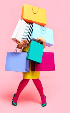 Parlak elbiseli tanınmayan bir kadın bir sürü alışveriş çantası taşıyor pembe stüdyo arka planında alışveriş poşetleri taşıyor. Moda konsepti, güzellik, satış elemanı, Kara Cuma, satış. kopyalama alanı. ad