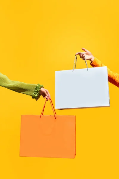 Sale offer. Black Friday. Shopping discount. Closeup of two girls hand holding purchase bags isolated on bright yellow background. concept of fashion, online shopping, salesperson. copy space. ad
