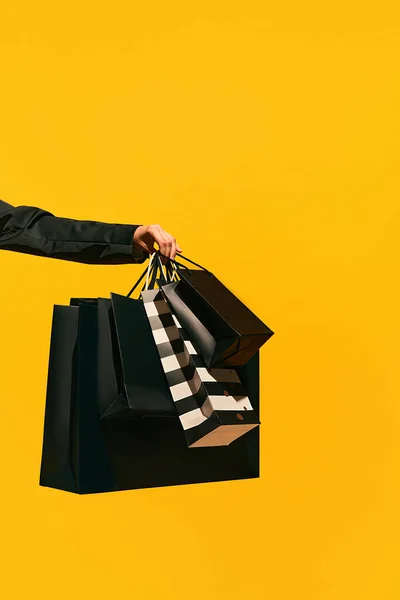 Sale offer. Black Friday. Shopping delivery. Closeup of womans hand holding purchase black bags isolated on bright yellow background. concept of fashion, beauty, salesperson. copy space. ad