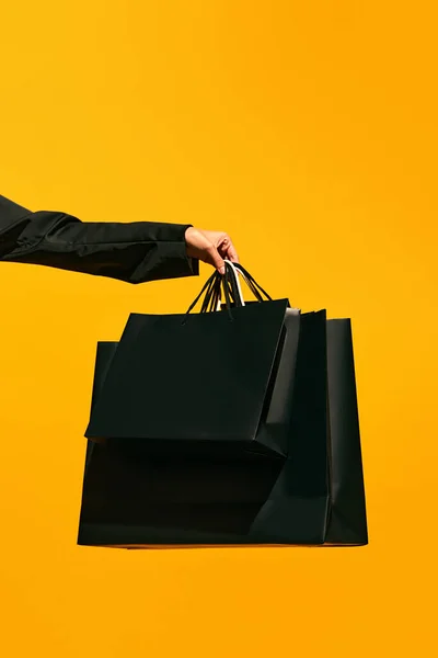 Sale offer. Black Friday. Shopping delivery. Closeup of ladys hand holding purchase black bags isolated on bright yellow background. concept of fashion, beauty, salesperson. copy space. ad
