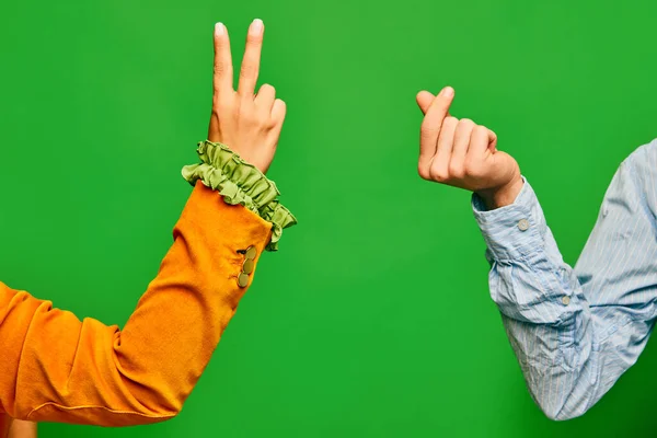 Poster. Two hands, male showing crossed fingers in heart shape, female demonstrate sign of peace isolated on green color background. Concept of vintage fashion, beauty, emotions, peace and love, ad.