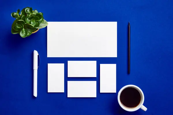 Corporate Identity Template Set. Business stationery layout template. Set of pen, pencil, envelope, card, paper, etc over indigo blue background with cup of coffee and plants. Concept of occupation.