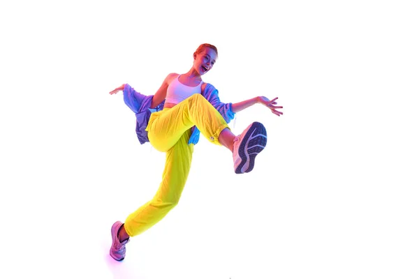 从下面全身上下都是快乐的年轻女子 穿着时髦的运动服跳舞 穿着运动鞋在霓虹灯下看着相机 运动的概念 积极的生活方式 复制空间 — 图库照片