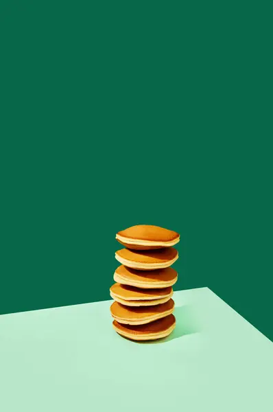 Breakfast time. Food pop art photography. Freshly prepared delicious sweet pancakes over green background. Minimalism style. Complementary colors. Concept of food, art, cooking, fashion. Ad