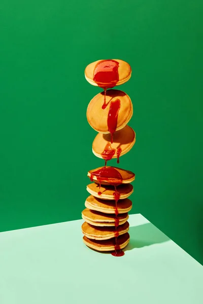 Food pop art photography. Close up. Flying sweet pancakes with delicious jam over green background. Vintage, retro 80s, 70s style, interior. Complementary colors. Concept of food, art, cooking. Ad