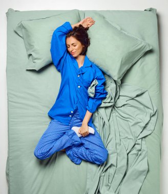 Genç, güzel bir kadın, gözleri kapalı yatıyordu. Yatağında mavi pijamalarıyla yatıyordu. Şekerleme, dinlenme, dinlenme, uyku zamanı, iyi uykular, sabah, akşam. ad