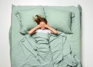 Üst Manzara. Küçük güzel kız uyanmak için elleriyle gözlerini kapadı. Neşeli çocuk, çocuk büyük bir nane yatağında dinleniyor. Uyku sağlığı kavramı, insan dokunuşu, uyanma, aşk, haz, uyku zamanı. Ad