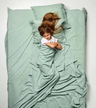 Üst Manzara. Battaniyeyle kaplanmış küçük üzgün kız ellerini çaprazladı ve somurttu. Üzgün çocuk, büyük bir nane yatağında çocuk. Duygu kavramı, uyku sağlığı, insan dokunuşu, uyanma, aşk, haz, uyku zamanı. Ad