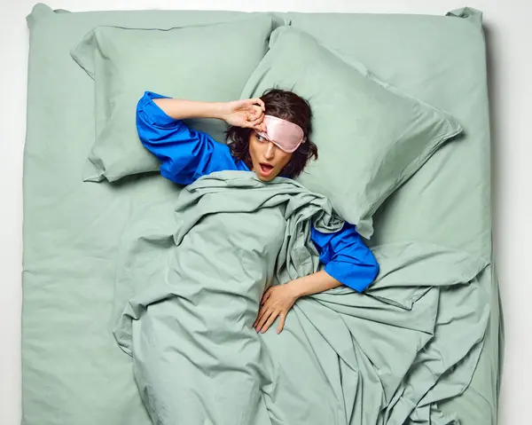 Young beautiful woman with sleeping mask covered with blanket watching who already wakeup. Enough night sleep. early morning. Concept of recreation, rest, bedtime, sleep wellness, home. ad