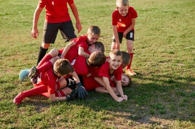 Futbolcu çocuklar futbol sahasında, çimenler hareketli, gol atan oyuncuların ardından sevinçle oynuyorlar. Futbol oynuyordum. Spor yaşam tarzı, hobiler, boş zaman aktiviteleri. Ad.