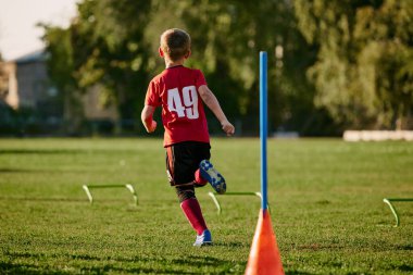 Çocuğun arka görüntüsü, spor üniformalı futbolcu koşuyor, antrenman yapıyor, futbol sahasında maç öncesi futbol çipleriyle antrenman yapıyor. Sağlıklı yaşam tarzı, hobiler, boş zaman aktivitesi kavramı. Ad