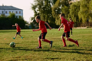 Çocukların tam boy fotoğrafı, spor üniformalı futbolcular güneşli yaz gününde futbol sahasında maç öncesi topla antrenman yapıyorlar. Spor konsepti, aktivite, hobi. Ad